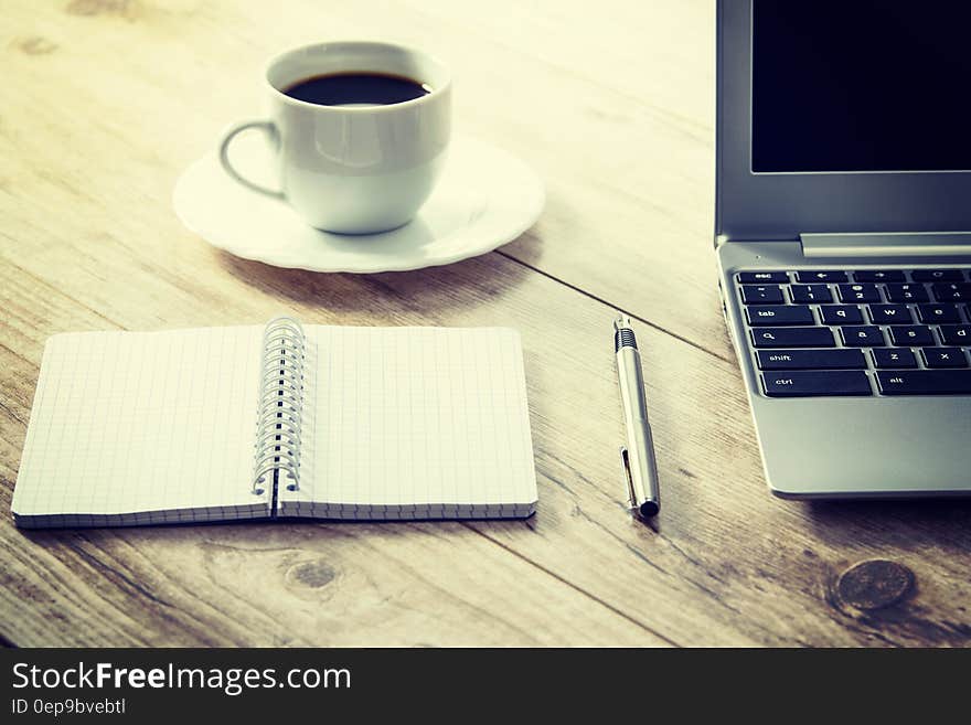 White Ceramic Cup on White Round Saucer Near Spiral Notebook