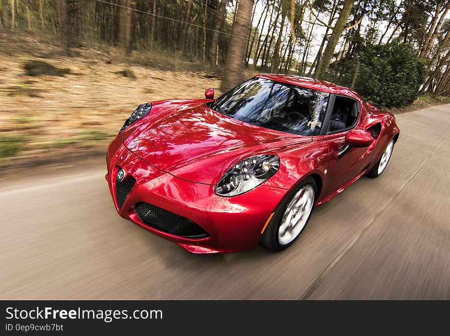 Red sports car blurred in motion driving down road through forest on sunny day. Red sports car blurred in motion driving down road through forest on sunny day.