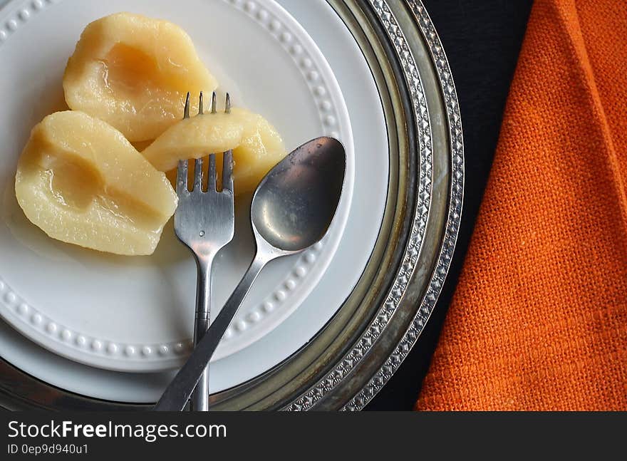 Overhead view of pear halves on white china plate with fork and spoon on chargers with orange napkin. Overhead view of pear halves on white china plate with fork and spoon on chargers with orange napkin.