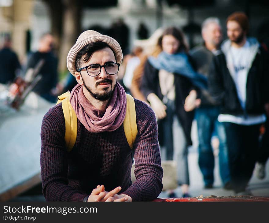 Man Sitting Next to Couple of Person Walking on the Street during Daytime