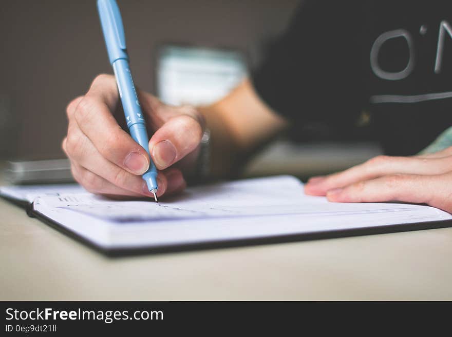 Person Holding Blue Ballpoint Pen Writing in Notebook