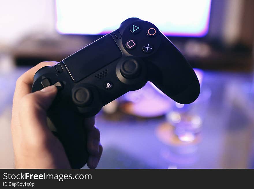 Close up of hand holding gaming console in front of television set inside home.