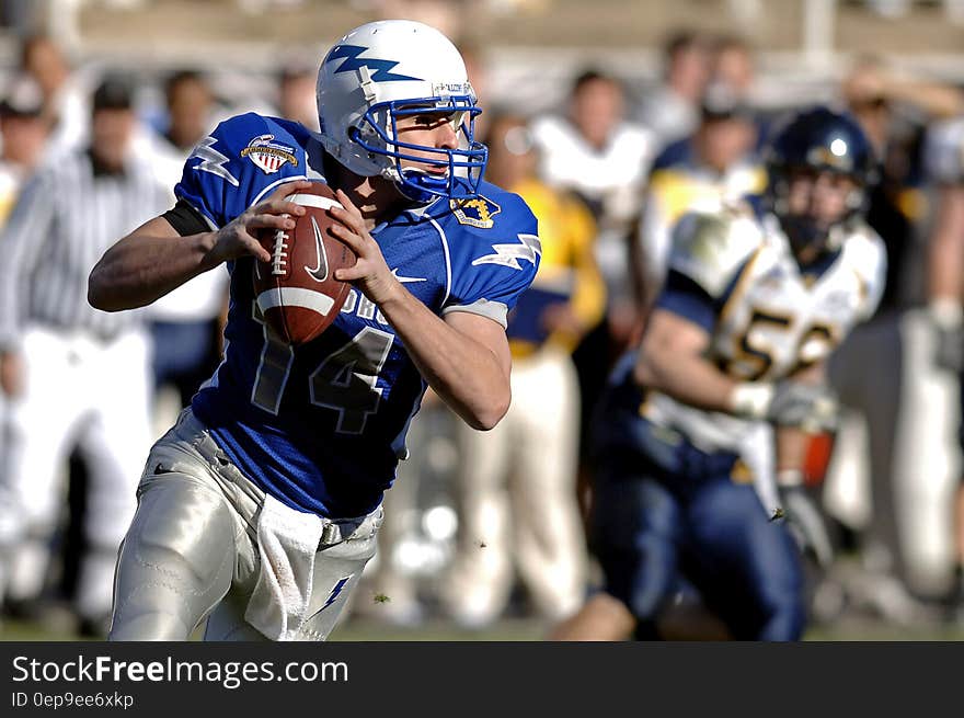 American football player holding ball while running during game. American football player holding ball while running during game.