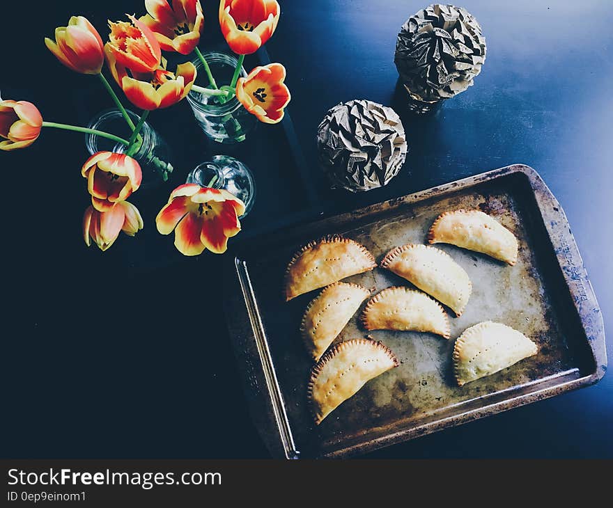 Yellow and Red Flower on Clear Glass Flower Vase Beside Brown Steel Tray With Pastry