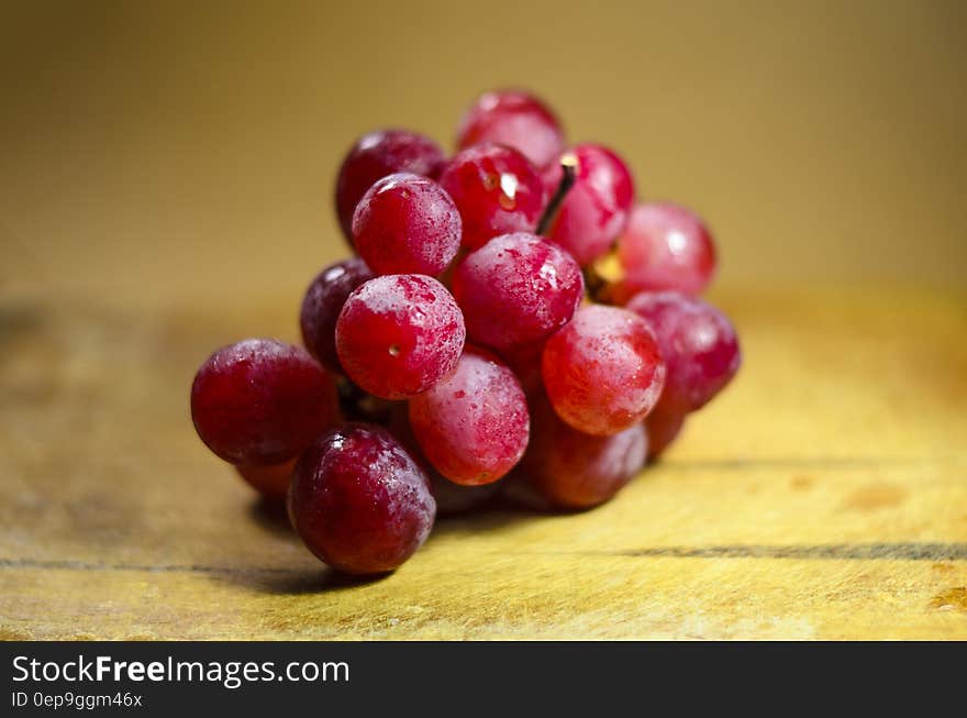 A bunch of fresh red grapes glistening in the light closeup with selective focus and a yellow wooden background.