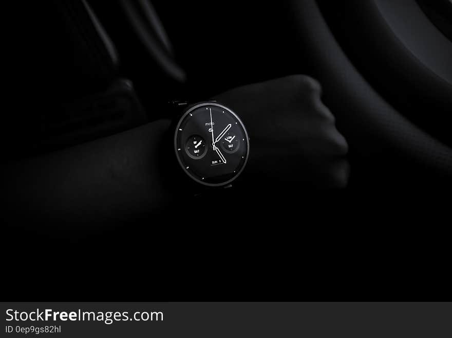 Stylish modern wristwatch in front of shadowed hand on black background.