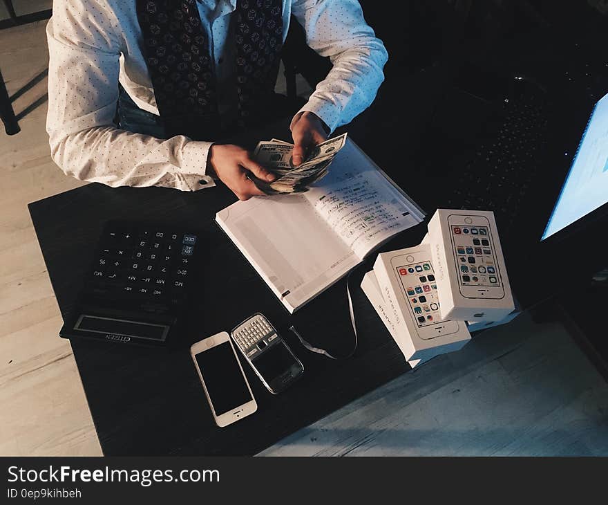 Person Counting Money With Smartphones in Front on Desk