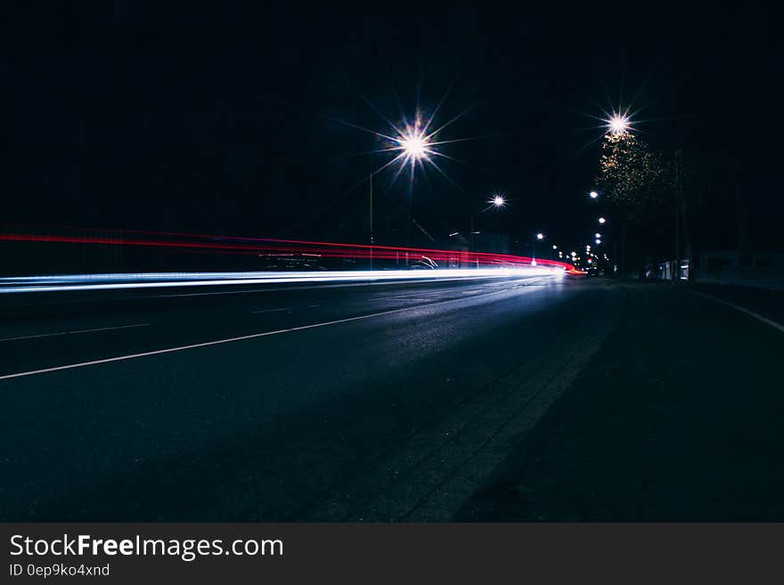 Highway with bright white car headlights approaching and another vehicle with its rear lights receding and with two bright overhead lights illuminating an otherwise black night. Highway with bright white car headlights approaching and another vehicle with its rear lights receding and with two bright overhead lights illuminating an otherwise black night.