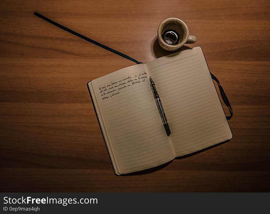 Pen on Notebook Beside a Teacup on Brown Wooden Plank