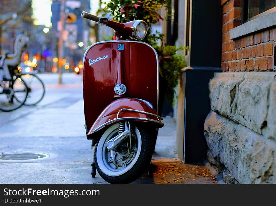 Red Vespa scooter parked outside brick building on city sidewalk at twilight. Red Vespa scooter parked outside brick building on city sidewalk at twilight.