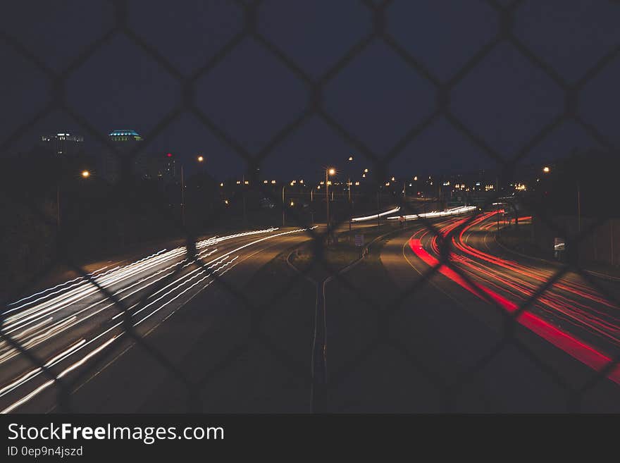 View from a bridge over the highway at night with vehicles coming towards the bridge on the left and traveling away from it on the right leaving white and red trails from car headlights and rear lights. View from a bridge over the highway at night with vehicles coming towards the bridge on the left and traveling away from it on the right leaving white and red trails from car headlights and rear lights.