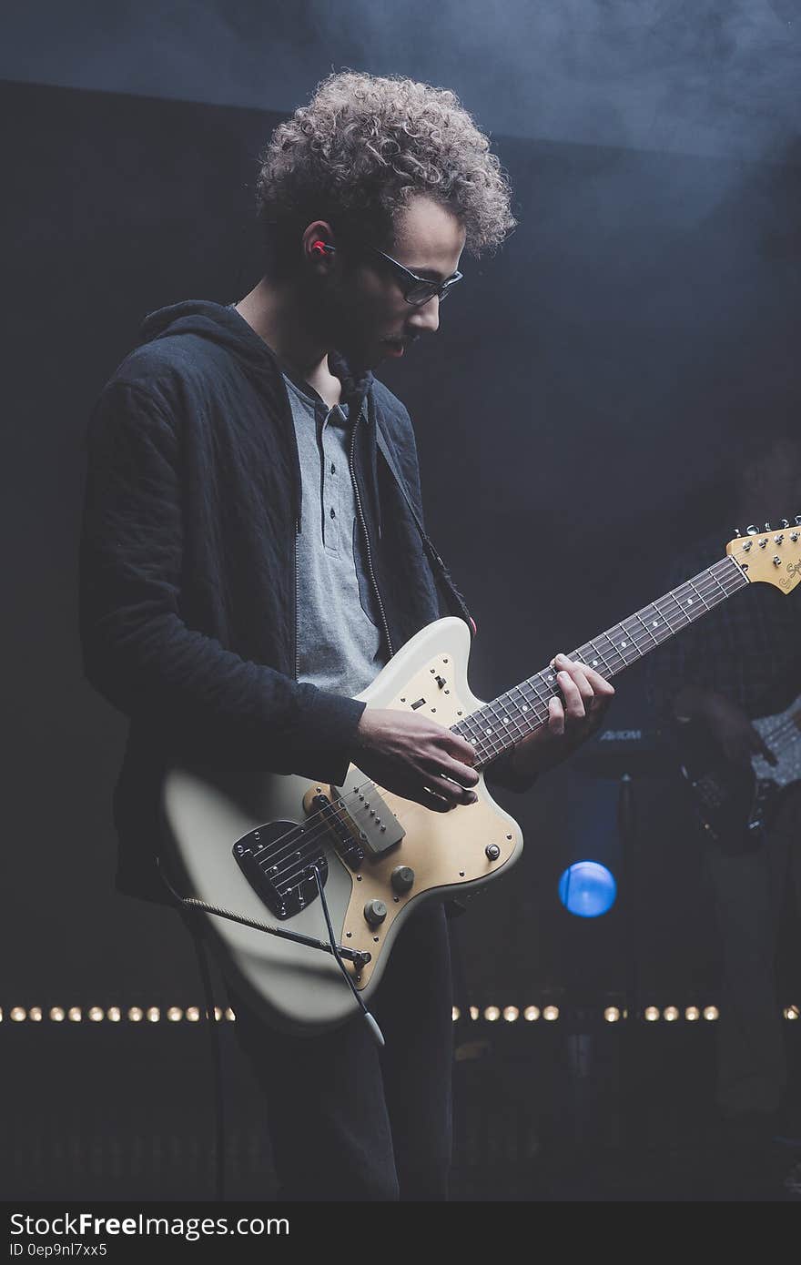 Guitarist with punk rock band playing electric guitar on stage, black background.