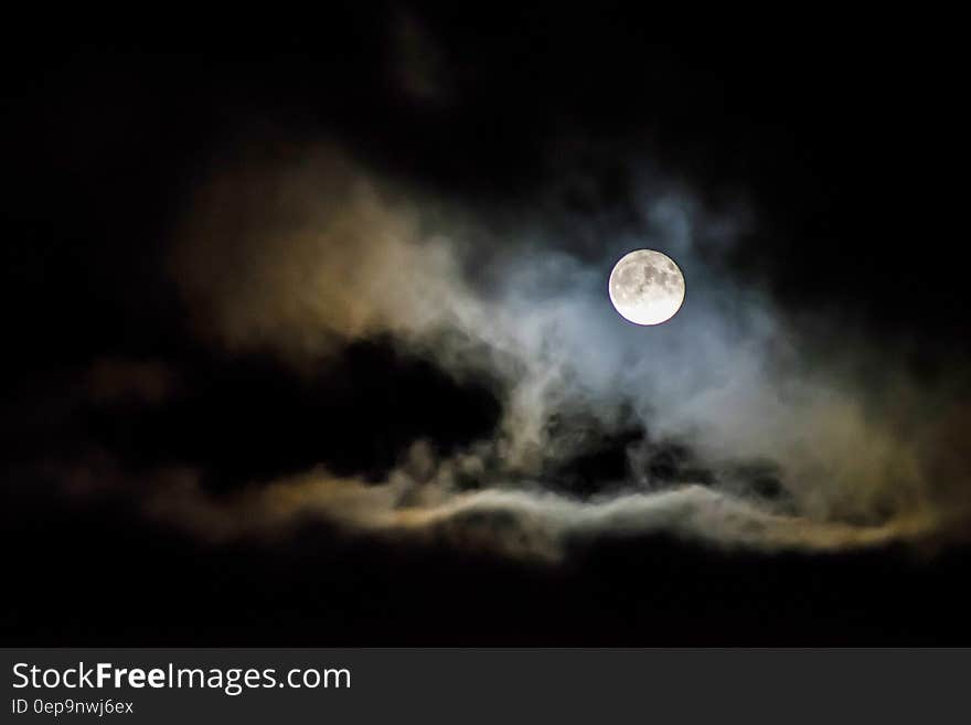 A full moon behind clouds in the night sky.