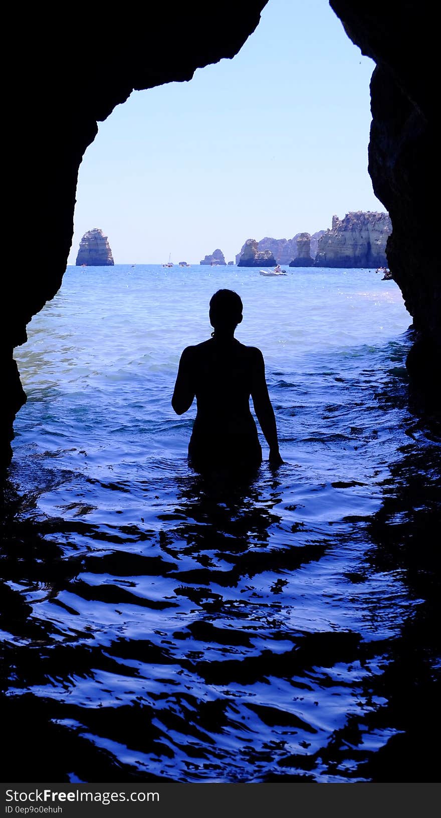 Silhouette of Woman at Blue Sea Inside Black Cave during Daytime