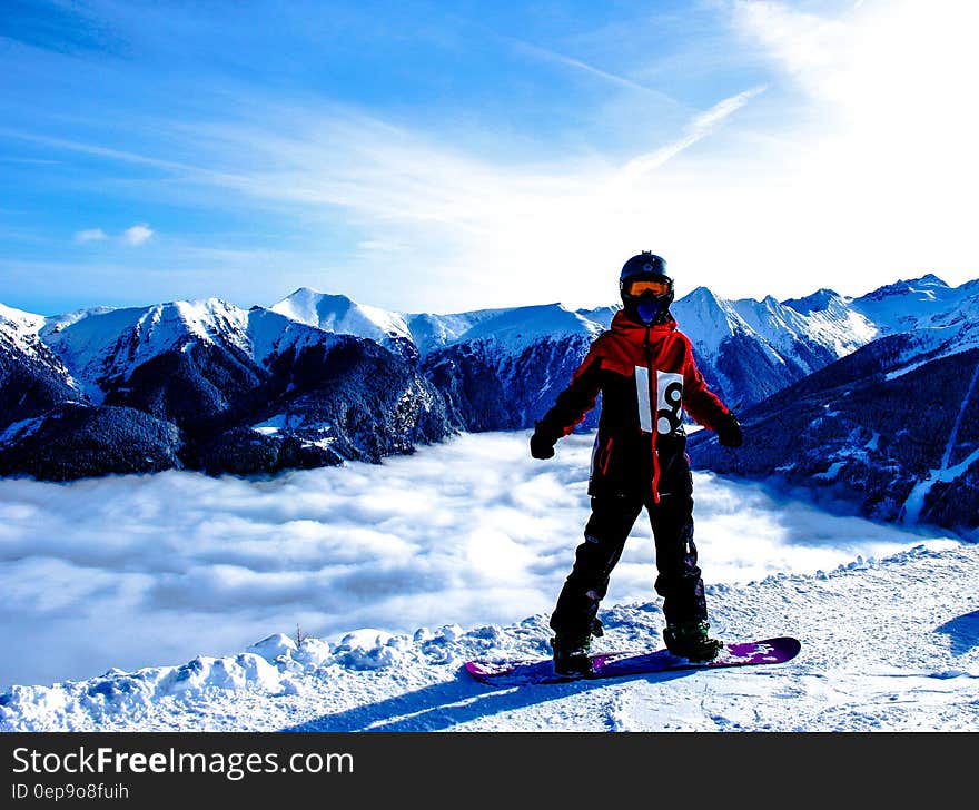 A snowboarder standing on a mountain peak, a spectacular view of the mountain range behind him.