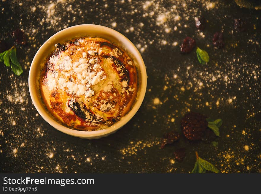 Overhead view into china ramekin with blueberry muffin sprinkled with powdered sugar. Overhead view into china ramekin with blueberry muffin sprinkled with powdered sugar.