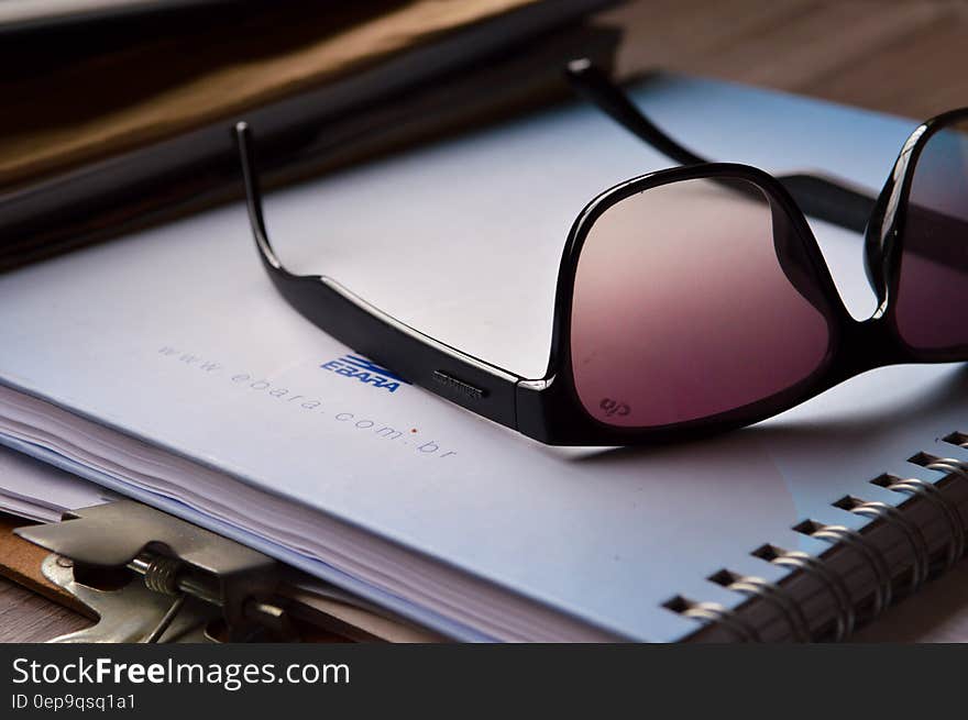 Close up of sunglasses on notebook and clipboard on wooden desk.