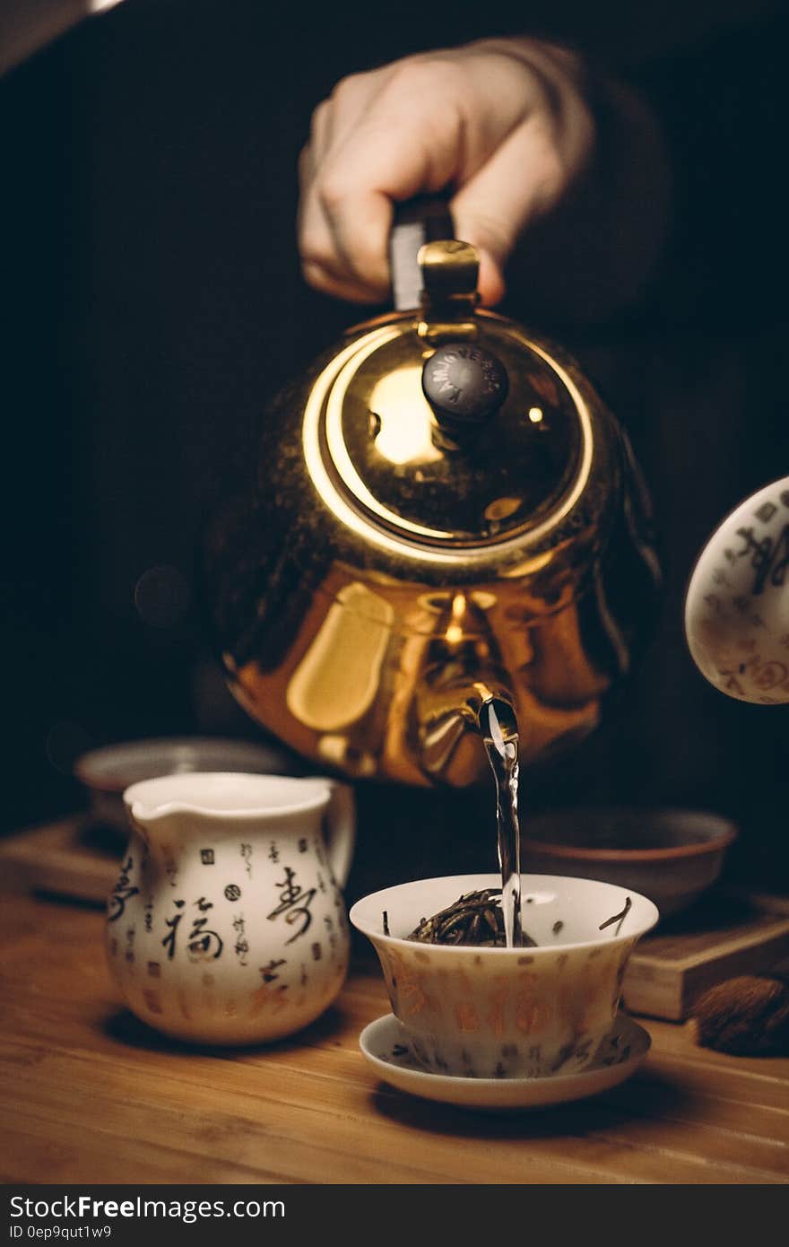 Person Holding Gold Teapot Pouring White Ceramic Teacup