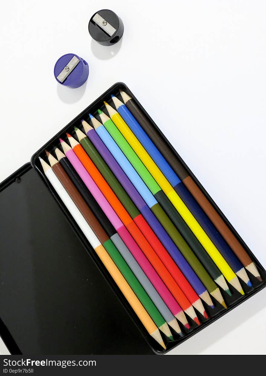 Black case with colorful pencils and sharpeners on white. Black case with colorful pencils and sharpeners on white.