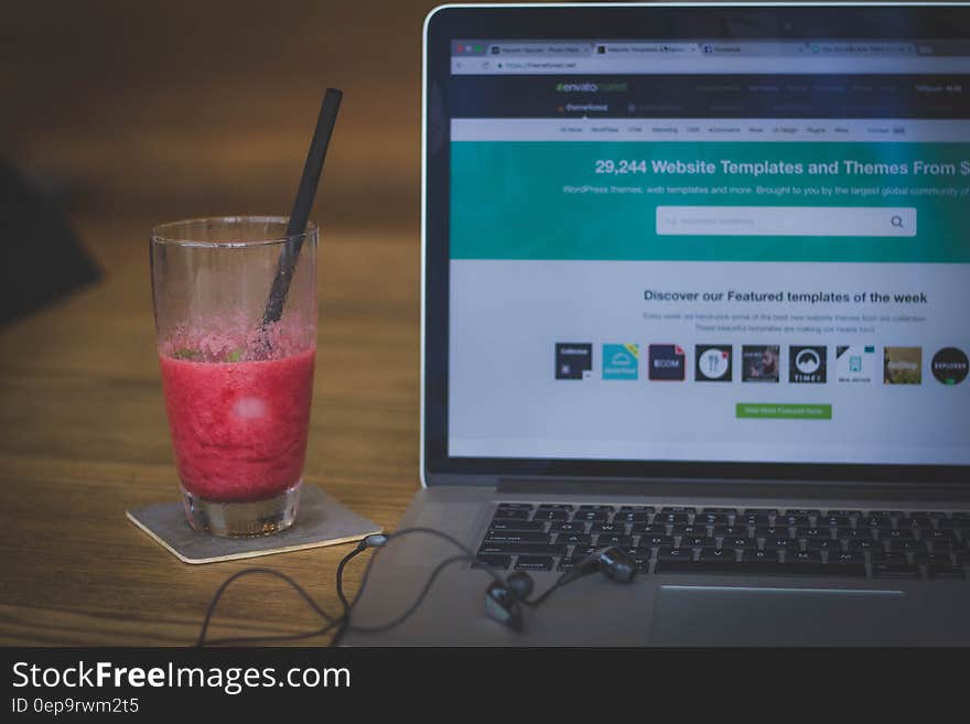 Laptop computer with open internet browser next to smoothie in glass with straw on wooden desktop. Laptop computer with open internet browser next to smoothie in glass with straw on wooden desktop.