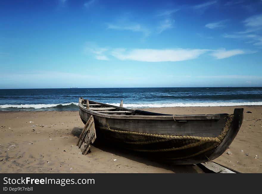 Wooden boat sitting in sand on beach against blue skies on sunny day. Wooden boat sitting in sand on beach against blue skies on sunny day.