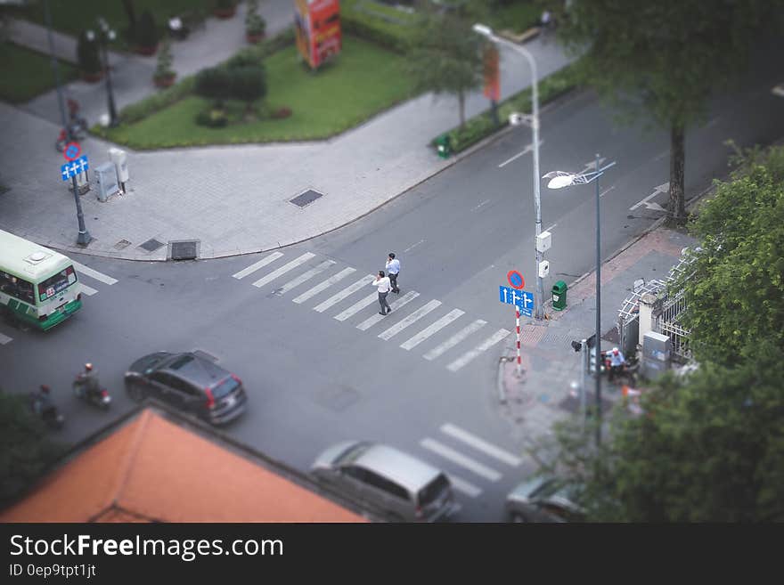 Aerial view of pedestrians in crosswalk at city intersection with traffic on sunny day.