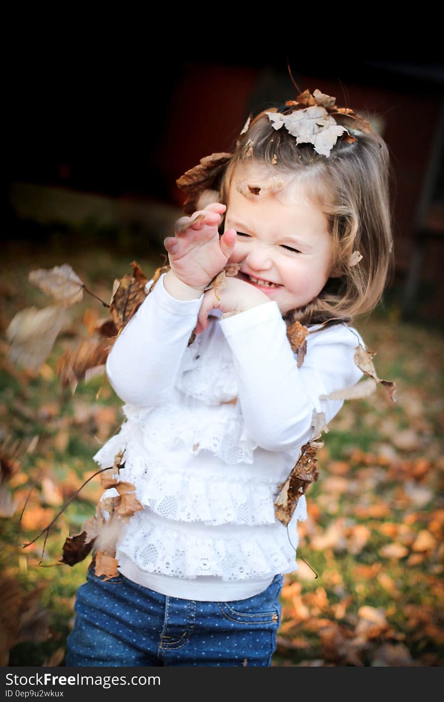 Focus Photo of Girl in White Long Sleeve Shirt With Brown Leaf on Her Head