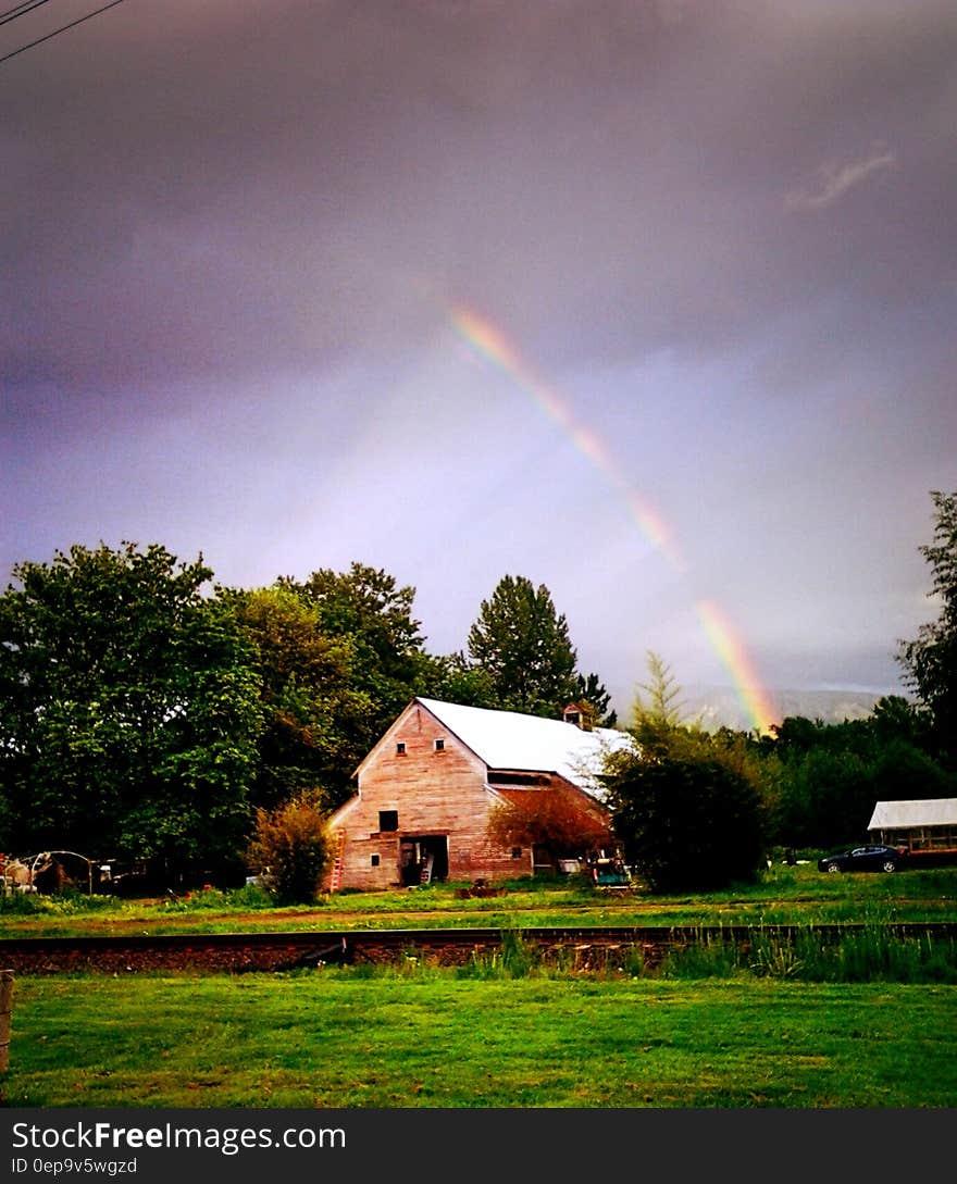 Rainbow in stormy skies over wooden barn in green field in countryside. Rainbow in stormy skies over wooden barn in green field in countryside.