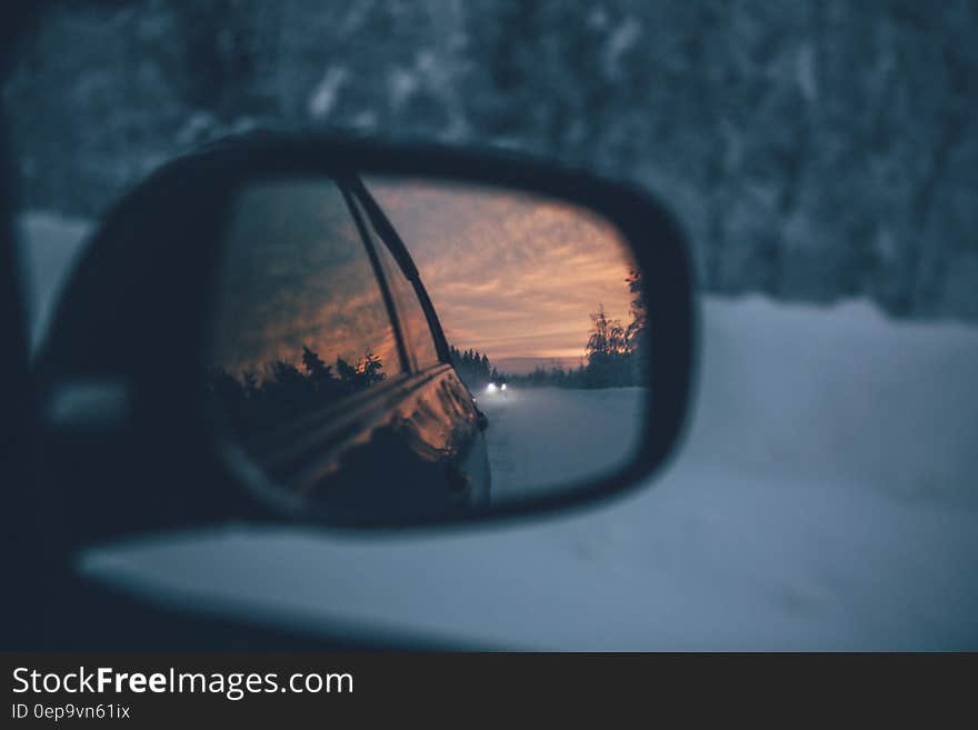 Rear view mirror on car reflecting sunset over snowy countryside. Rear view mirror on car reflecting sunset over snowy countryside.