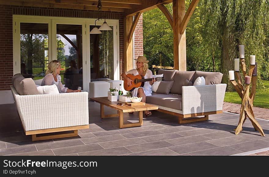 Women sitting on outdoor patio furniture playing guitar on sunny day. Women sitting on outdoor patio furniture playing guitar on sunny day.