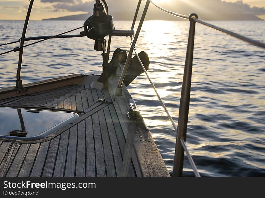 Bow of wooden boat sailing on waters with island on horizon at sunset. Bow of wooden boat sailing on waters with island on horizon at sunset.