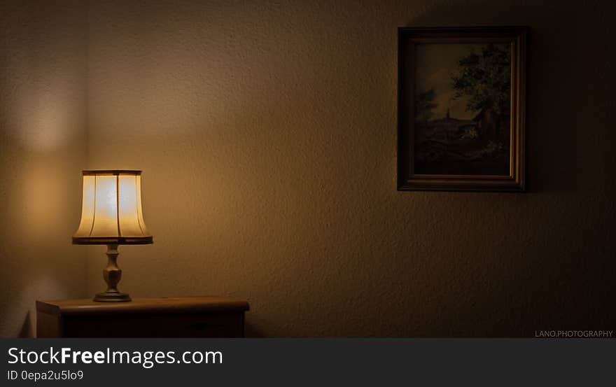 Lamp illuminated in dark room with table and painting. Lamp illuminated in dark room with table and painting.