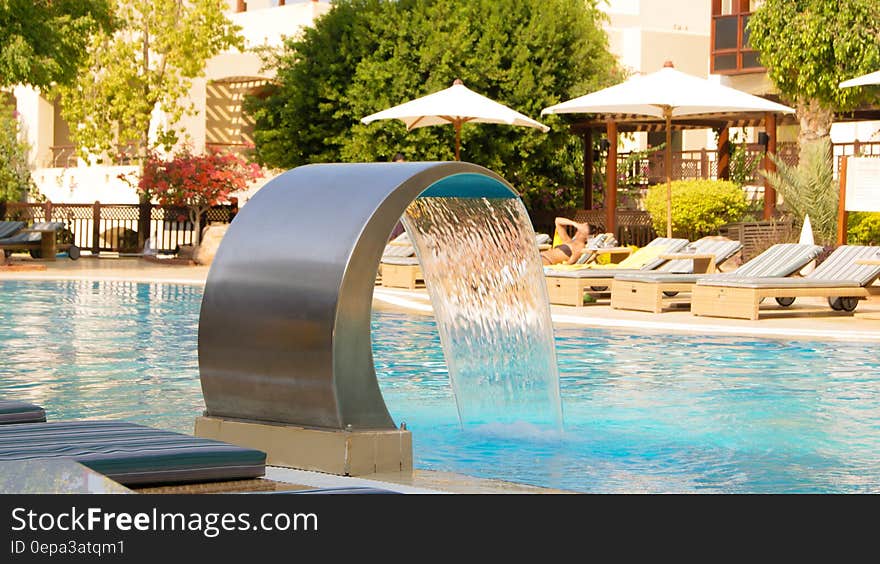 Water fountain cascading into hotel swimming pool with sunbeds and parasols in background. Water fountain cascading into hotel swimming pool with sunbeds and parasols in background.