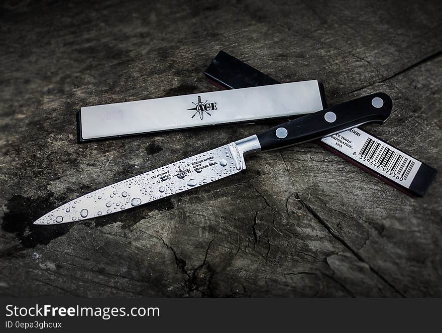 Drops of water on kitchen knife next to case on dark wooden background.