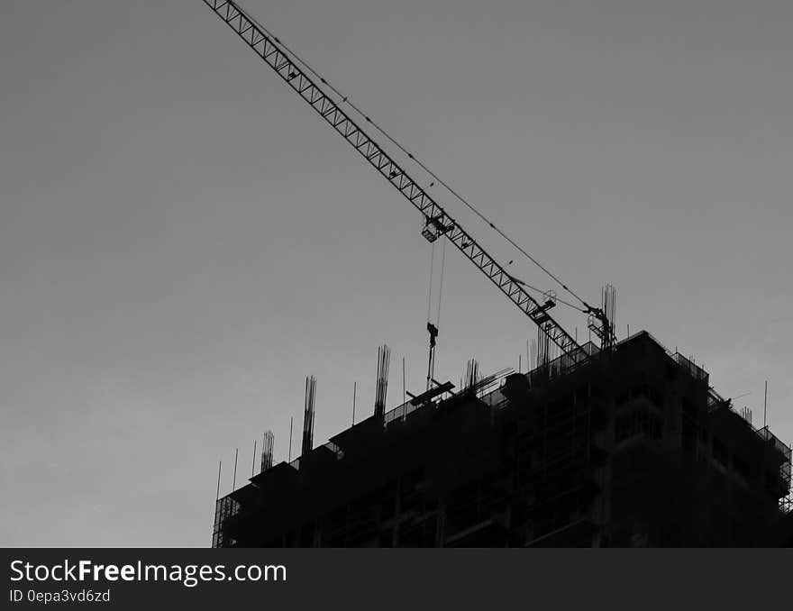 Crane on rooftop of modern building under construction silhouetted in black and white. Crane on rooftop of modern building under construction silhouetted in black and white.