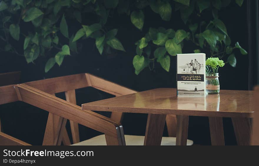 Book and vase of flowers on wooden table with chair nestled in plants. Book and vase of flowers on wooden table with chair nestled in plants.