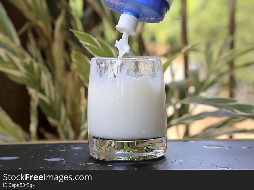 Glass of mild being filled from plastic squeeze bottle on table outdoors. Glass of mild being filled from plastic squeeze bottle on table outdoors.