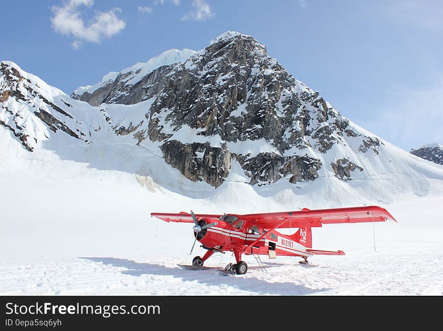 Biplane on snowy mountain peak with blue skies on sunny day.