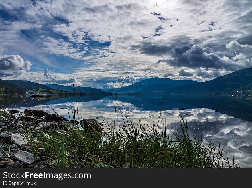 Clouds and blue skies reflecting in alpine lake in foothills of mountain range on sunny day. Clouds and blue skies reflecting in alpine lake in foothills of mountain range on sunny day.