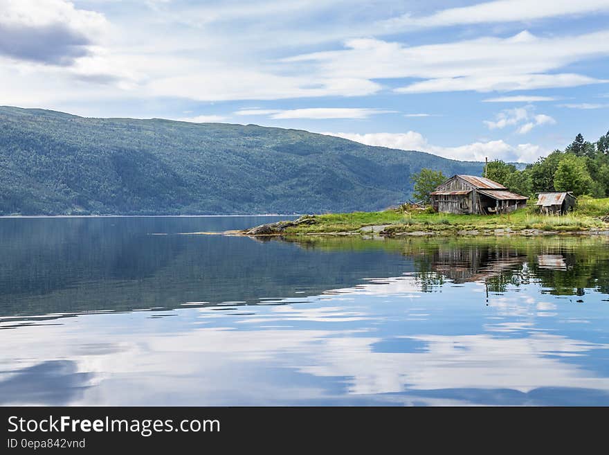 Rustic barn on shores of blue lake reflecting clouds and blue skies in hillside. Rustic barn on shores of blue lake reflecting clouds and blue skies in hillside.