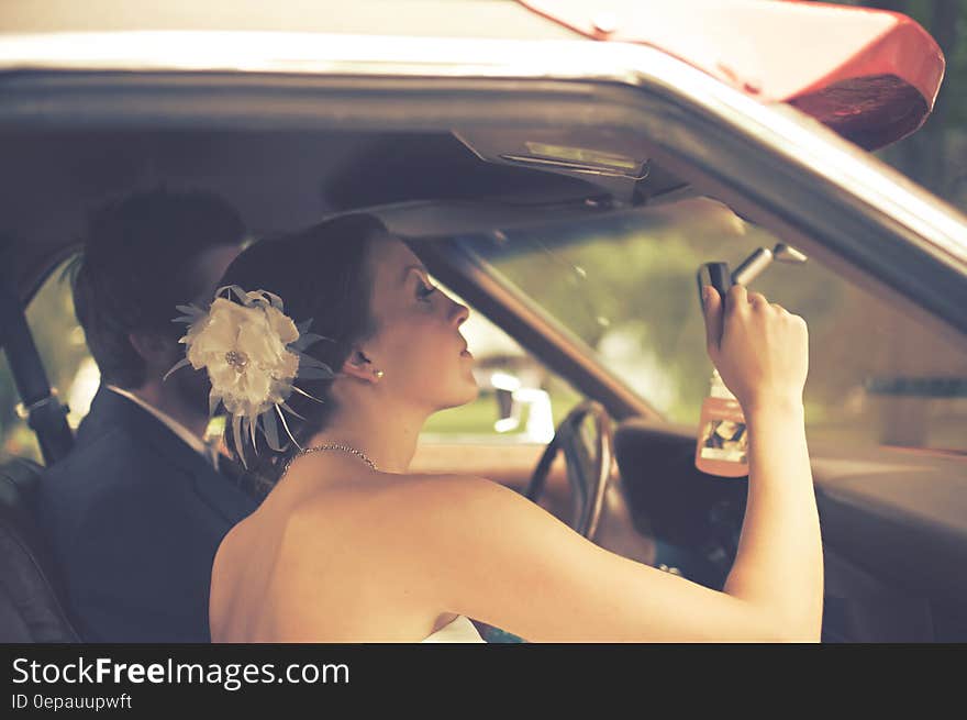 A young wedding couple sitting in a car, the bride looking at a rear mirror inside. A young wedding couple sitting in a car, the bride looking at a rear mirror inside.