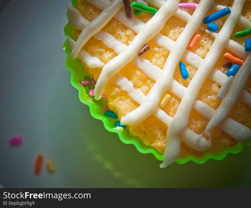 Close up of vanilla cupcake in green wrapper with white frosting and colorful sprinkles. Close up of vanilla cupcake in green wrapper with white frosting and colorful sprinkles.