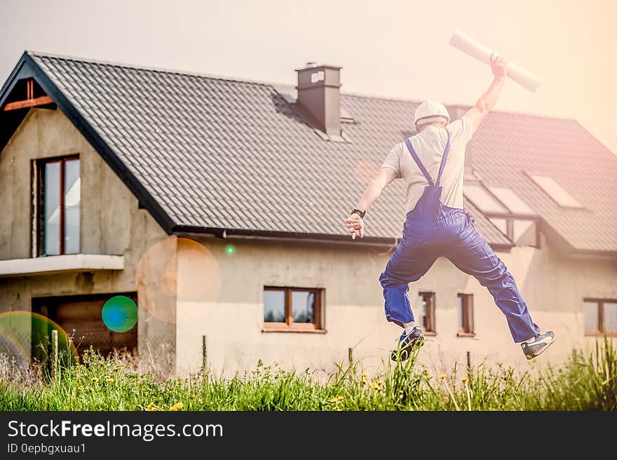 Construction worker or architect jumping for joy holding blueprints outside house on sunny day. Construction worker or architect jumping for joy holding blueprints outside house on sunny day.