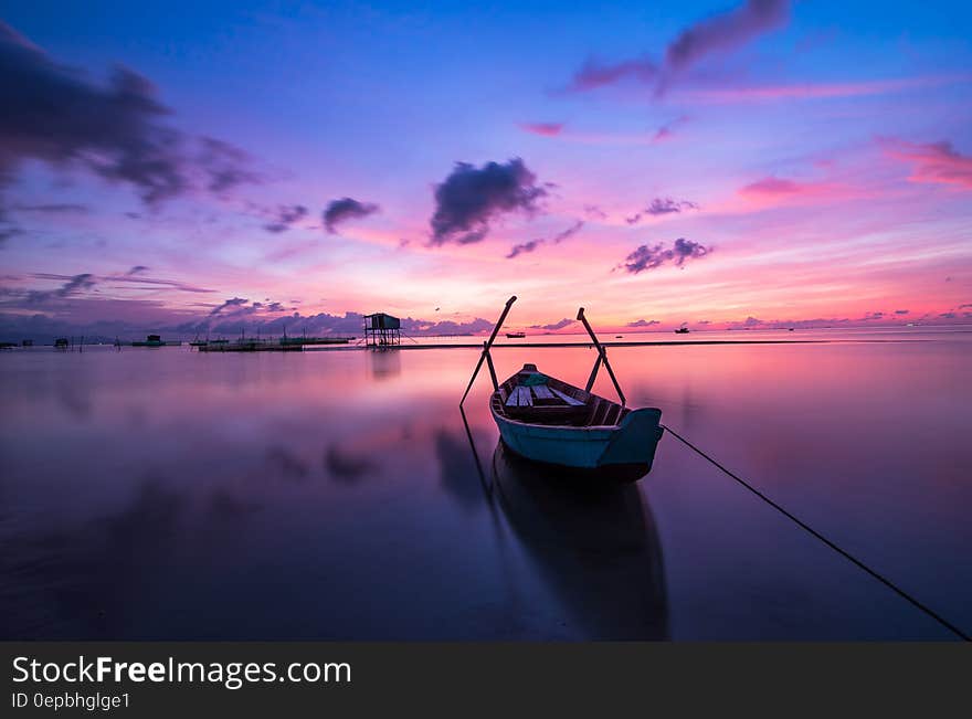 Wooden boat tied to shores in still waters of Vietnam at sunset with purple skies. Wooden boat tied to shores in still waters of Vietnam at sunset with purple skies.