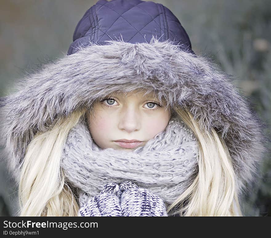 Portrait of blond haired girl in purple winter jacket and knit scarf outdoors.