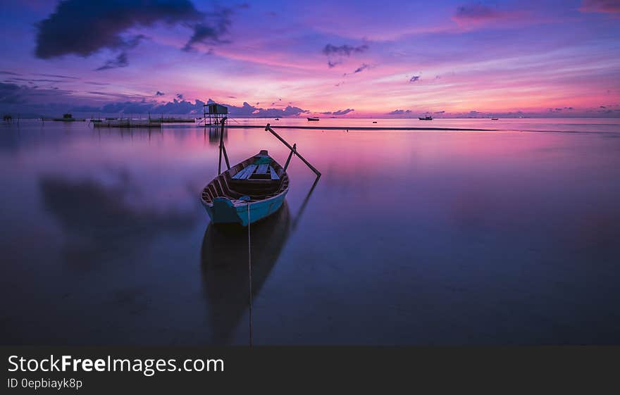 Wooden rowboat tied to shores in still waters at sunset with purple skies. Wooden rowboat tied to shores in still waters at sunset with purple skies.