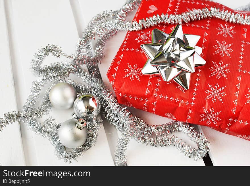 Red and silver wrapping paper on package with bow covered in garland and balls on white. Red and silver wrapping paper on package with bow covered in garland and balls on white.