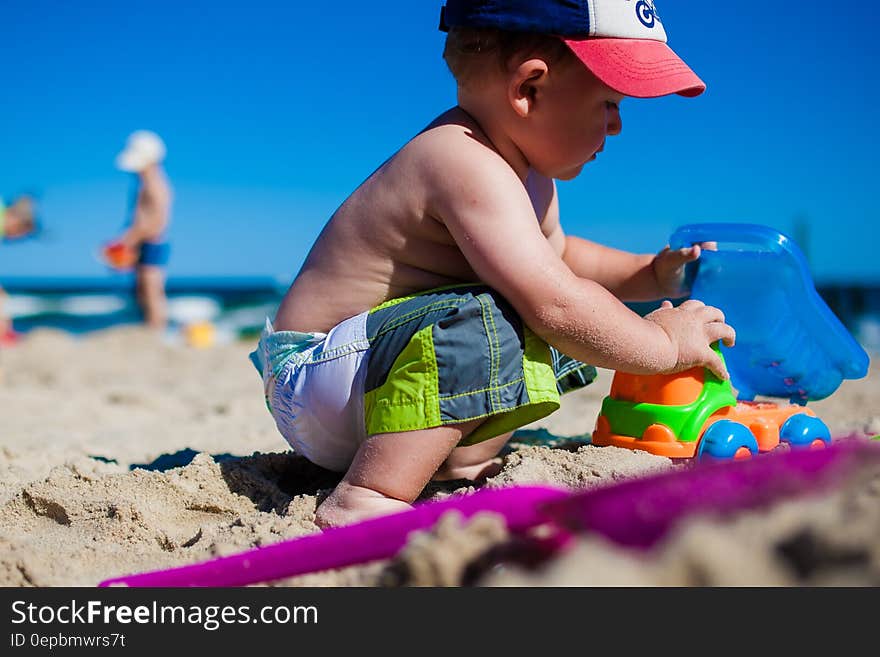 Side view of young boy playing with toys on sandy beach with blue sky and sea background. Side view of young boy playing with toys on sandy beach with blue sky and sea background.