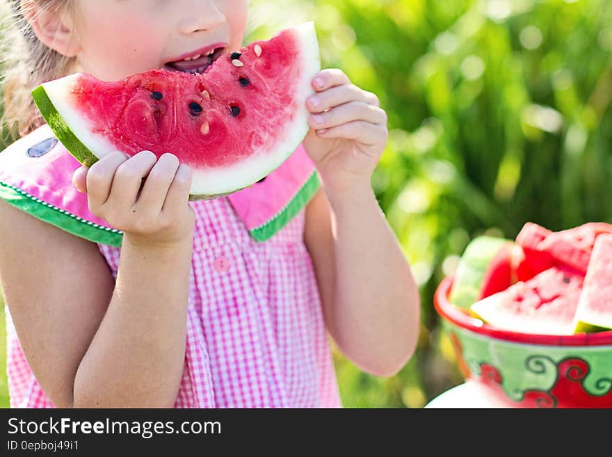 A young girl eating watermelon outdoors in the summer.