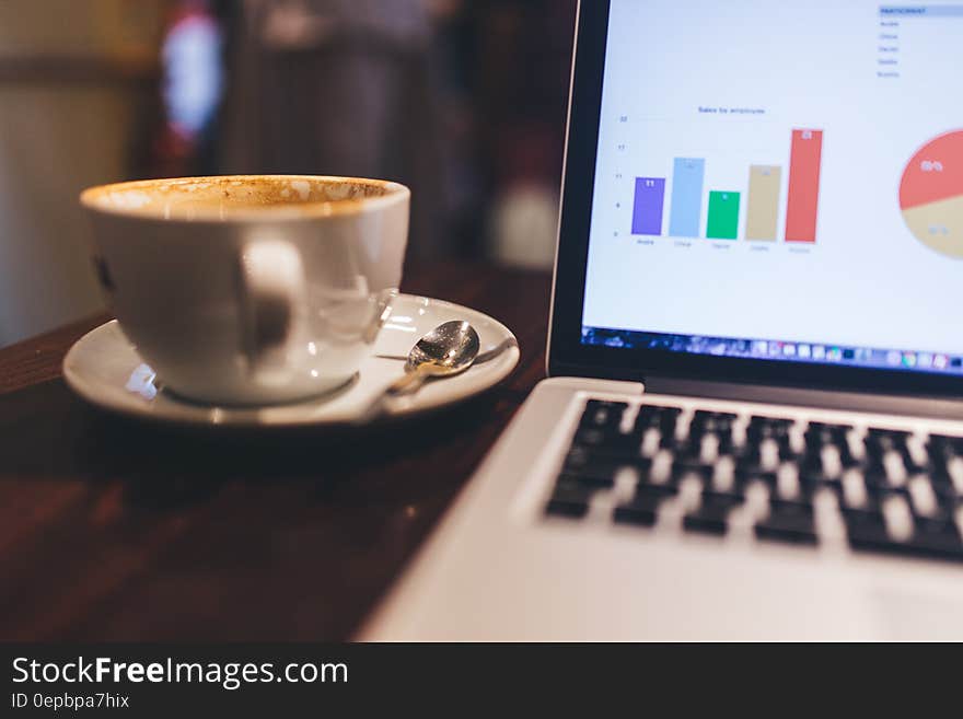 White Ceramic Tea Cup Beside White and Black Laptop Computer